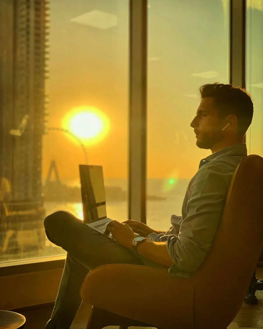 Nicolò Manica, founder of Cofoundle, working on his laptop by the window at sunset in Dubai